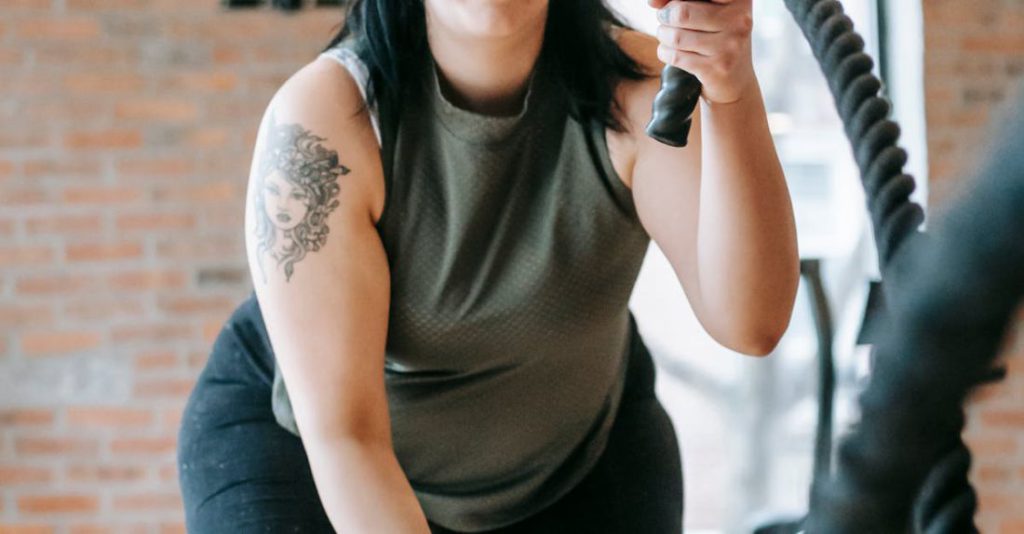Functional Fitness - Low angle of concentrated female in sportswear exercising with heavy battle ropes during intense functional training