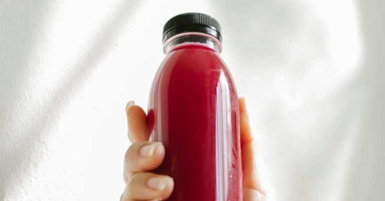 Body Detox - Unrecognizable woman holding bottle of red juice against white wall