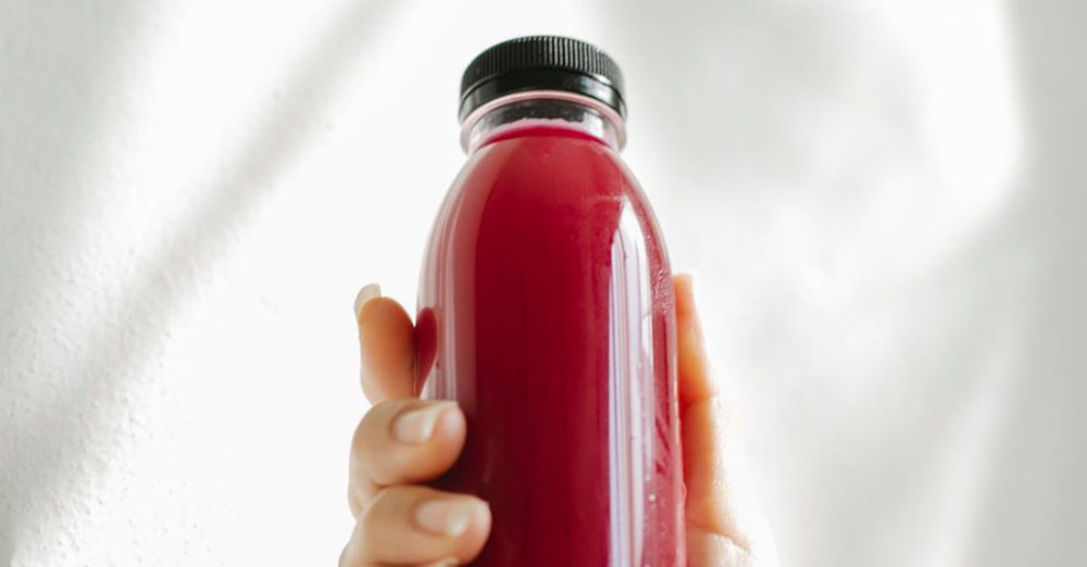 Body Detox - Unrecognizable woman holding bottle of red juice against white wall