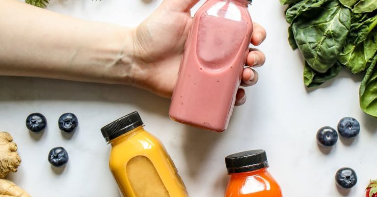 Detox Foods - Person Holding Bottle of Smoothie Beside Green Leaves, Carrots and Berries