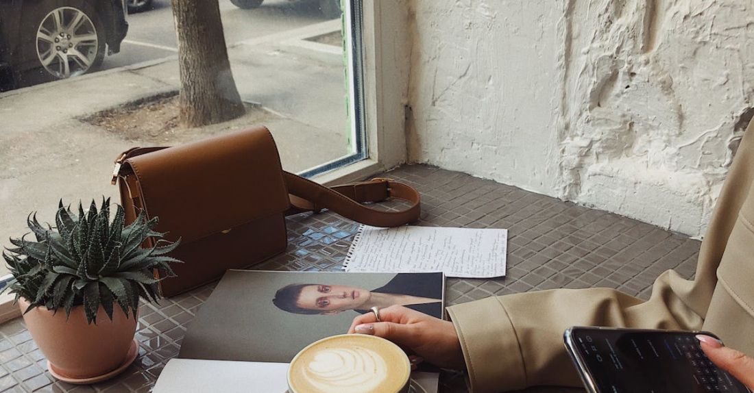 Weekend Detox - Crop of unrecognizable female tourist in casual wear surfing internet and flipping magazine while drinking coffee in sidewalk cafe