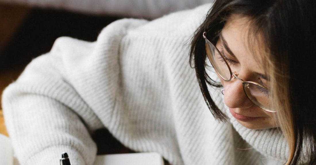 Sleep Schedule - From above of crop young female in warm clothes and eyeglasses writing plan for 2021 in notebook while sitting on floor near sleeping Akita Inu dog