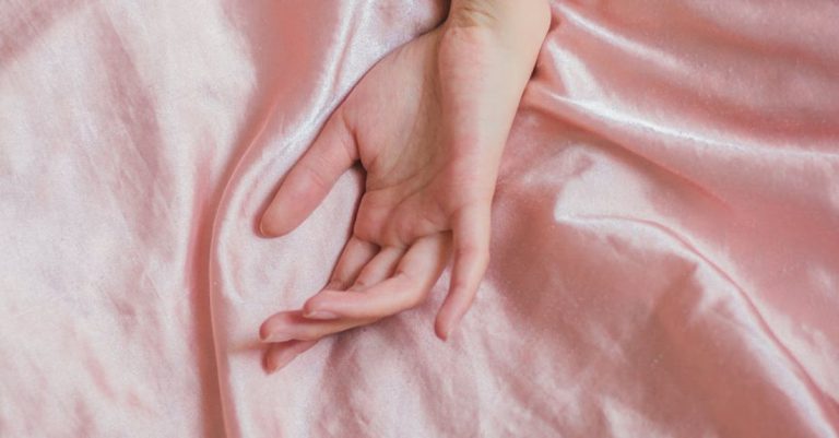 Sensitive Skin - Top view of hand of crop anonymous female on soft silk creased bed sheet at home
