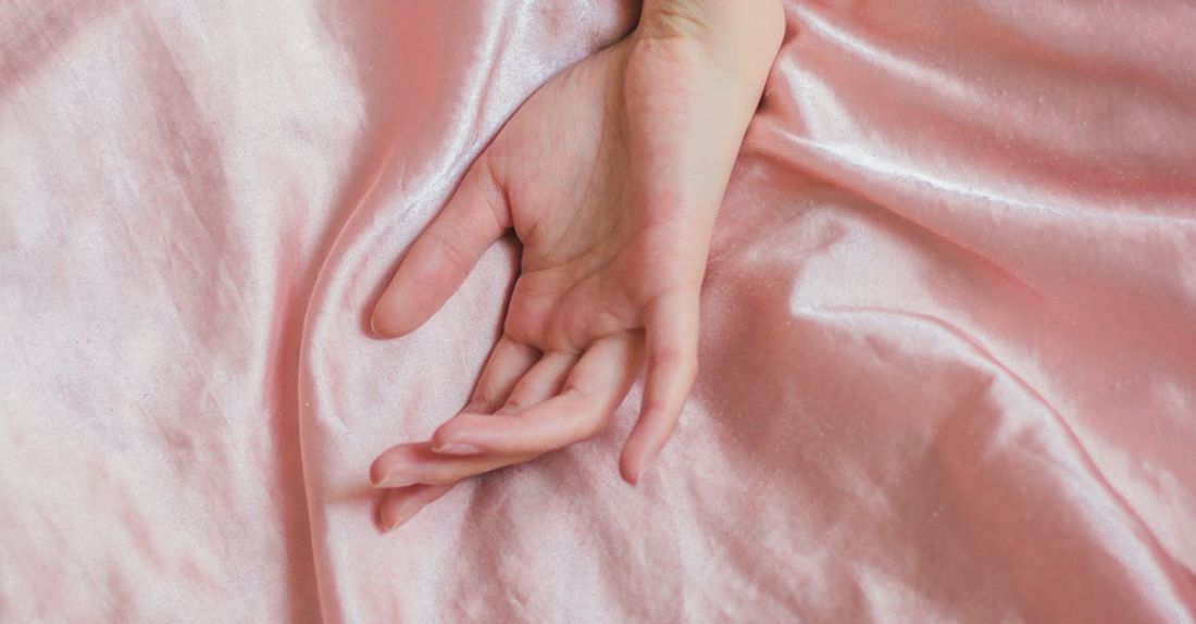 Sensitive Skin - Top view of hand of crop anonymous female on soft silk creased bed sheet at home